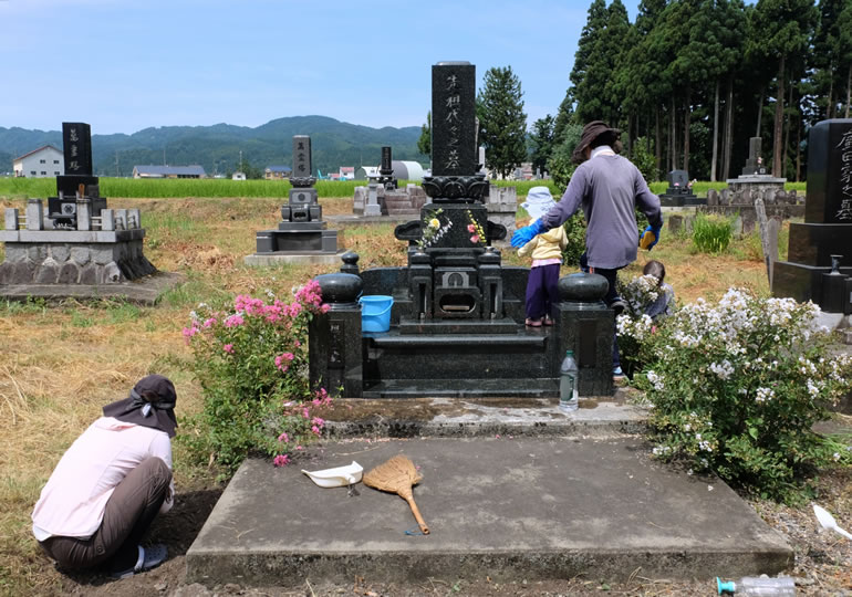 田舎のお墓を汗だくで手入れする高齢者と孫