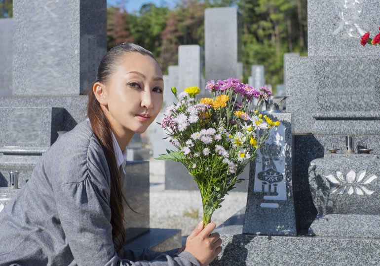 お墓の前で仏花を持つ女性