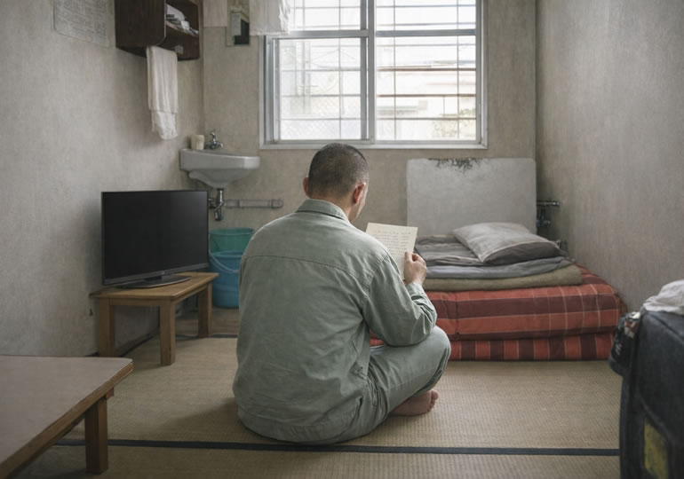 刑務所の部屋で手紙を読む受刑者の男性