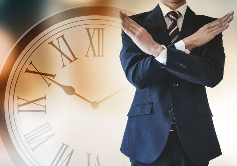 時計の前で腕でバツをする男性