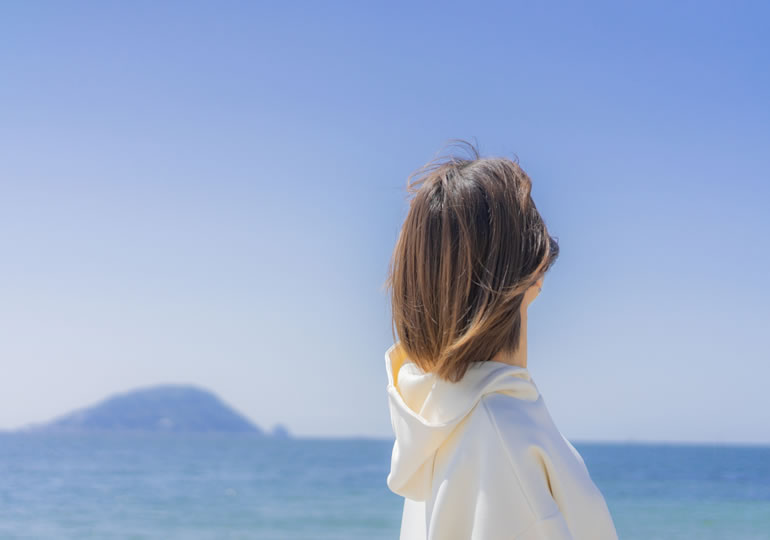 海洋散骨を検討しながら浜辺で空を眺める女性
