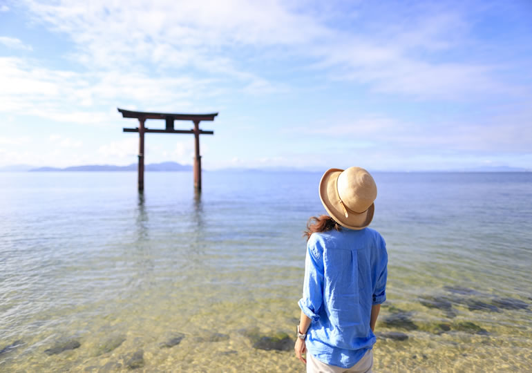浜辺の鳥居を見つめる女性の後ろ姿