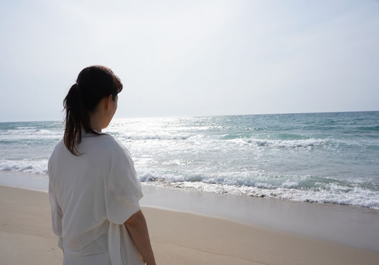 散骨した海を浜辺から見つめる女性