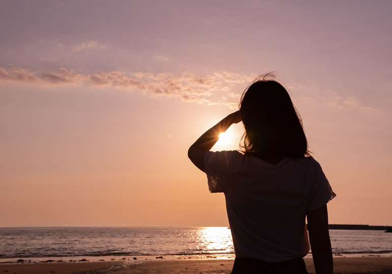 海洋散骨をした海と夕日を眺める女性の後ろ姿