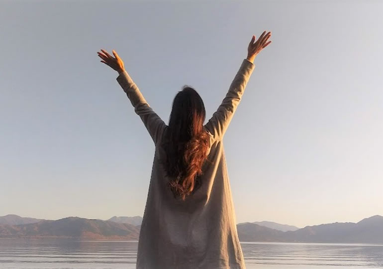 空を眺め両手を広げる女性