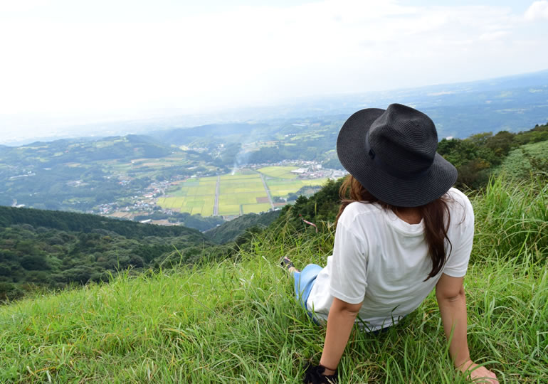 山の上から田園風景を眺める女性