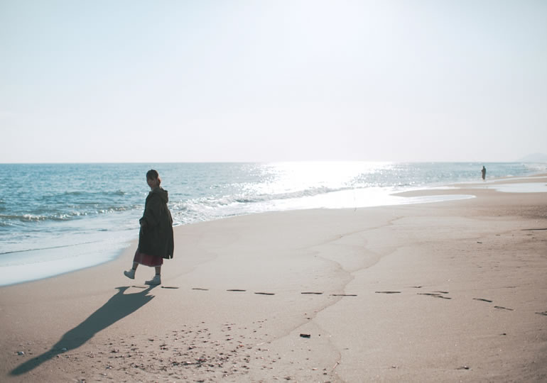 散骨した海を眺めながら砂浜を散歩する女性