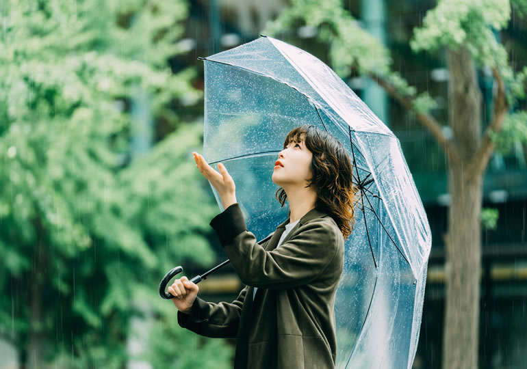 傘をさして手をかざし雨量を確かめる女性
