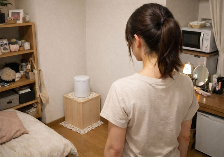 部屋に置かれた骨壺を見つめる女性