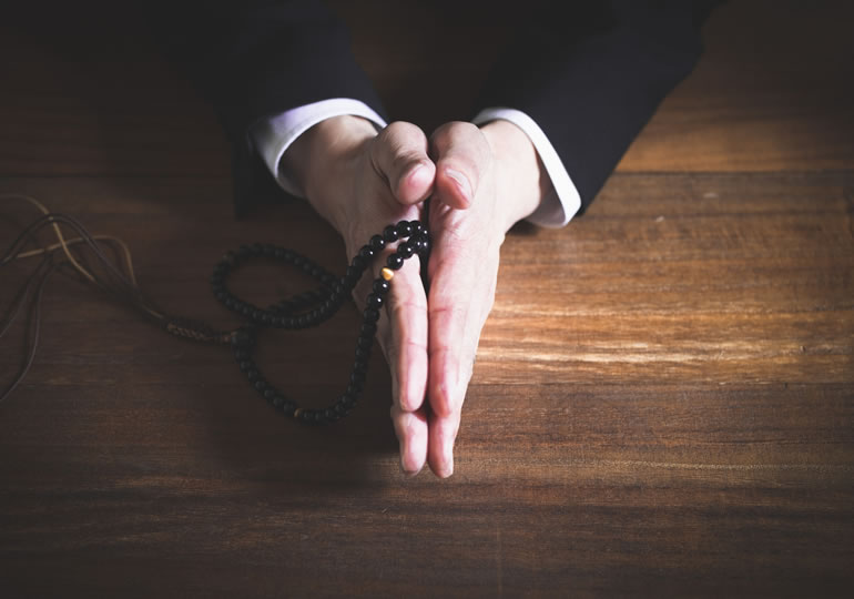 数珠を持って合掌する喪服の男性