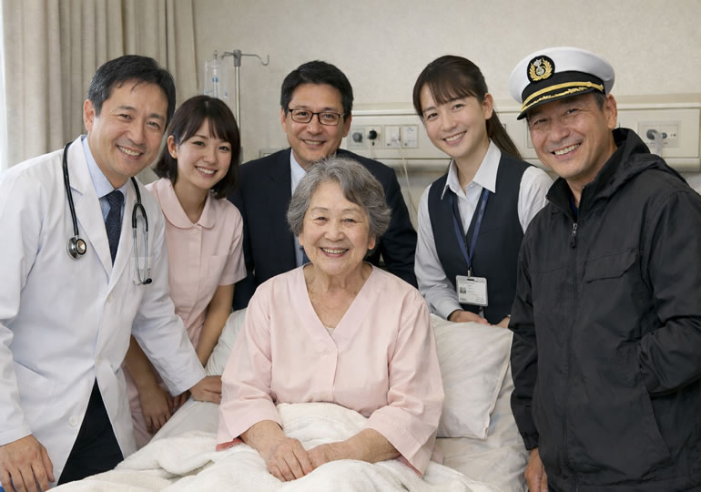 病院で笑顔の高齢女性を取り囲む笑顔の散骨関係者