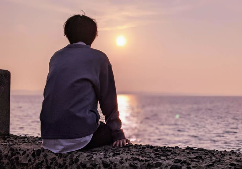 水平線の夕日を眺める少年