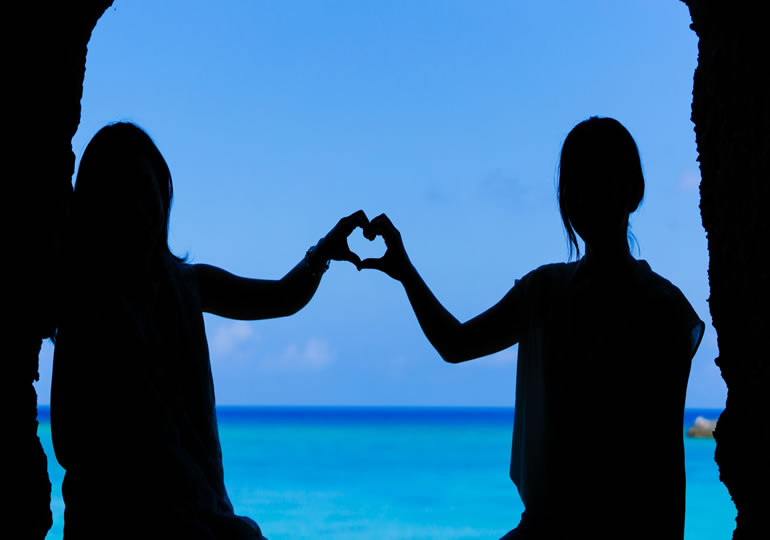 海を背景に指でハートを作る二人の女性