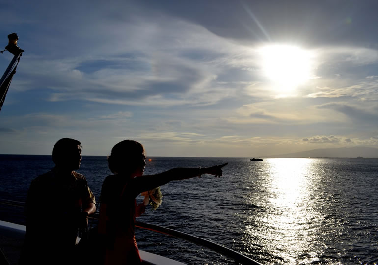 夕日をバックに散骨用の献花を持つ女性
