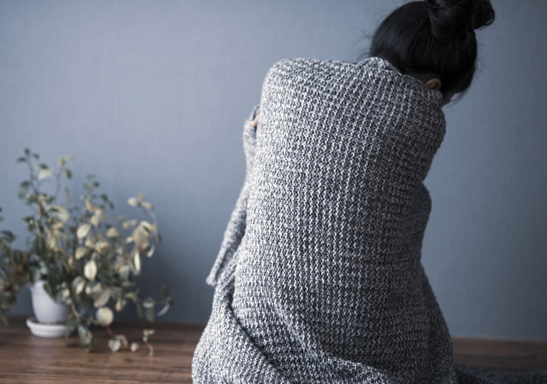 1人暮らしの部屋で悩む女性の後ろ姿
