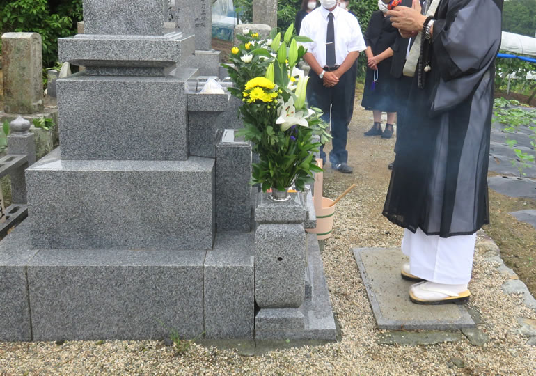 お墓の前でお経を読む住職と数珠を持ってお経を聞く檀家