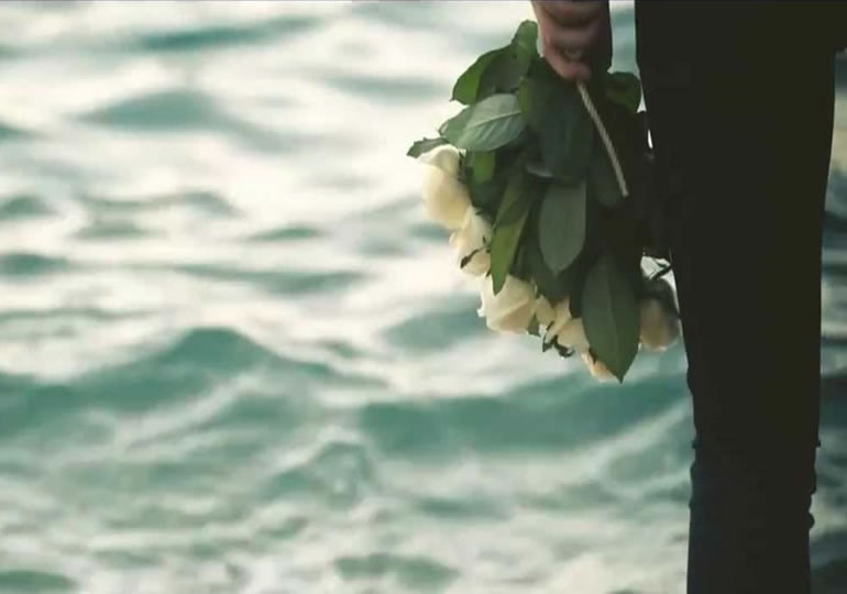 花束を持って散骨した海を見つめる男性