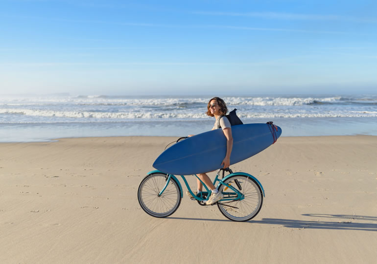 散骨した海の浜辺をサーフボードをもって自転車に乗る若い女性サーファー