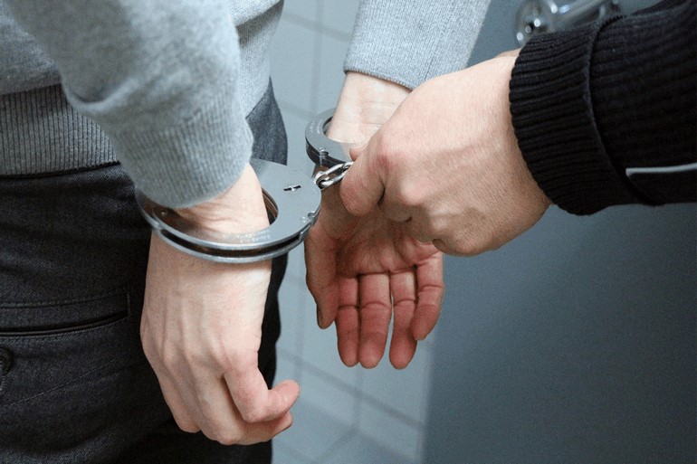 警察に逮捕され後ろ手に手錠を掛けられる男性