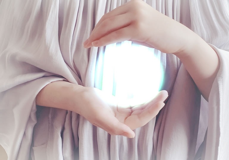両手で光を包み込む女性の手元